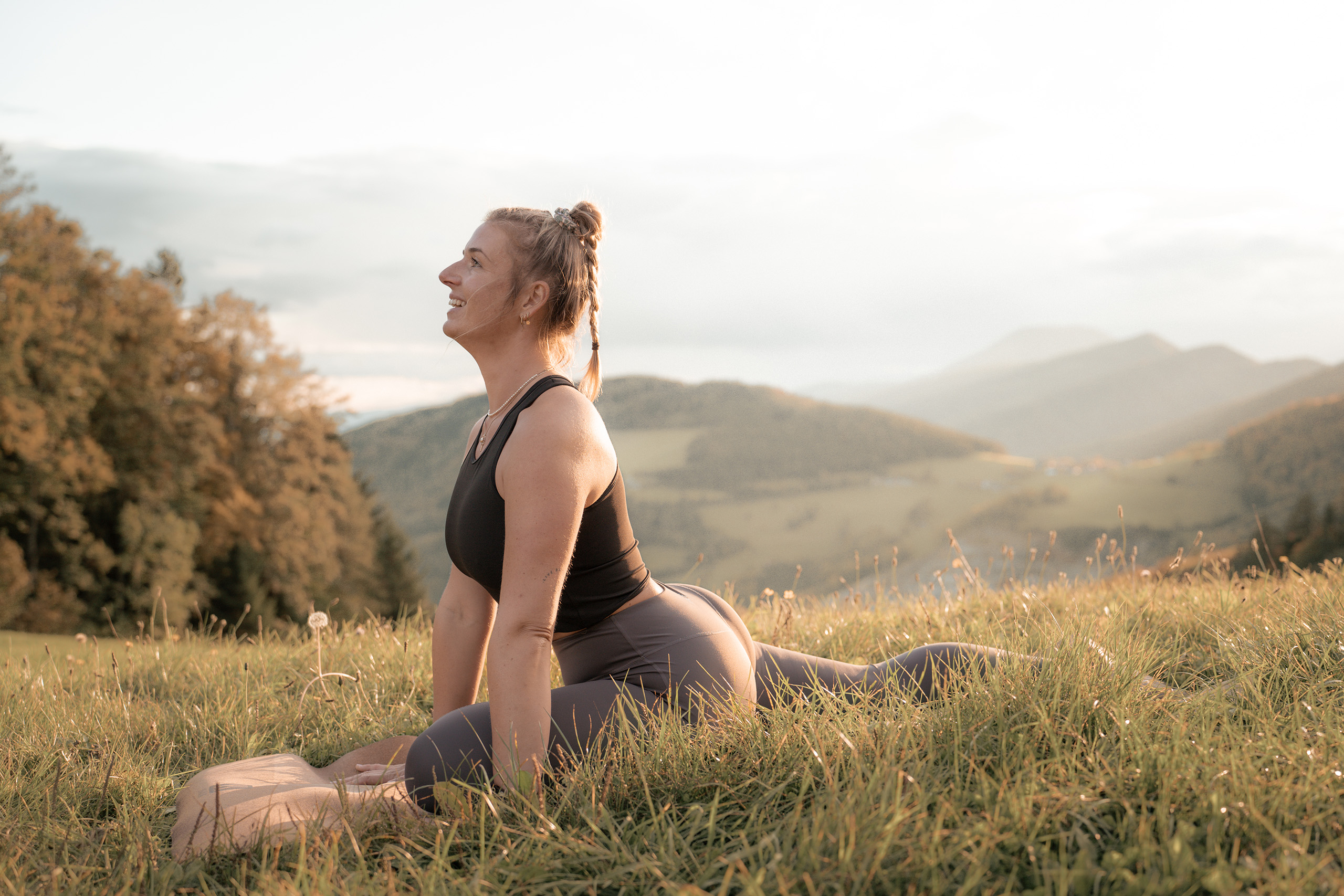 Kathi übt die Yoga-Taubenpose im Gras während einer JK_Traintogether-Session.